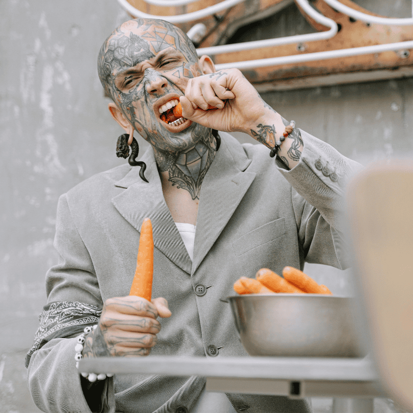 detalle de una persona con muchos tatuajes comiendo zanahorias